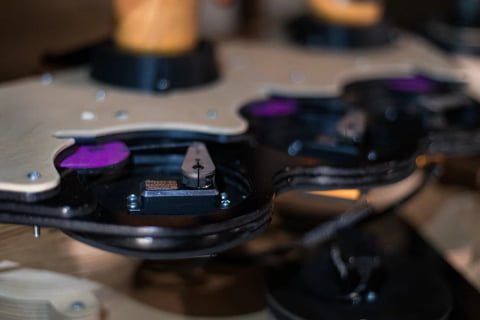 Close-up of the machinery beneath the pipes: a small motor and purple-tinted parts on layered wooden and black mounts.