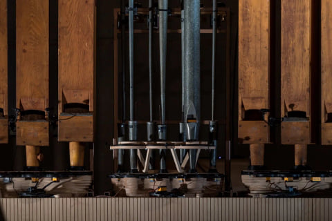Wooden pipes on either side of a cluster of metal pipes, each set on a robotic base.