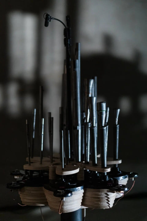 A cluster of thin metal pipes on a layered robotic base, lit against a dark wall.