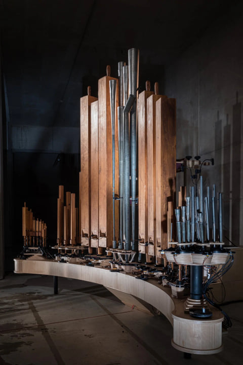 The instrument's wooden and metal pipes rising from its curved base in a dark room.