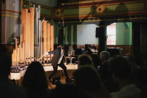 Navid Navab leaning toward the pipes during the concert, seen past the heads of the audience.