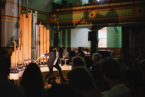 Navid Navab reaching toward the pipes during the concert, seen from within the audience.