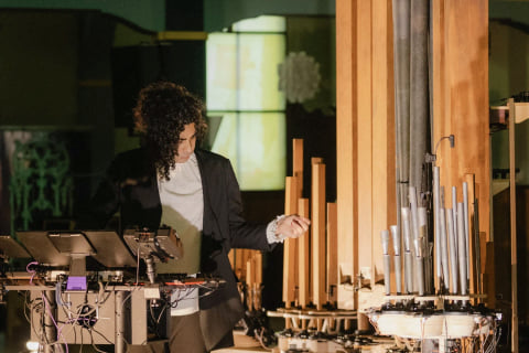 Navid Navab at a table of controllers beside the instrument's tall wooden and metal pipes.