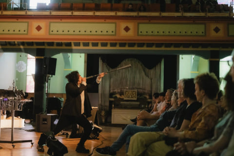 Navid Navab blowing into a long organ pipe like a horn, in front of a seated audience.