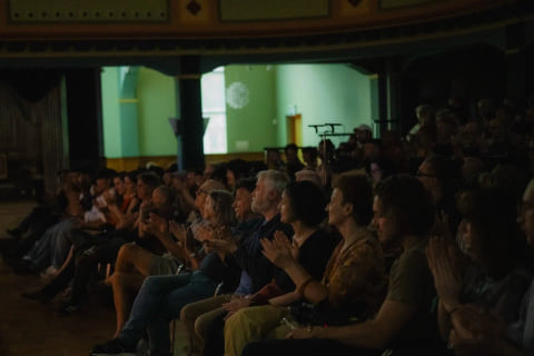 The audience applauding in a dimly lit hall.