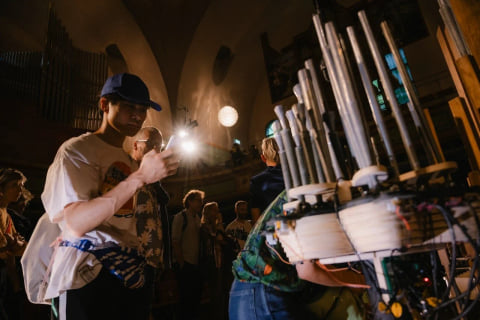Audience members looking closely at a cluster of the instrument's metal pipes, one lighting it with a phone.
