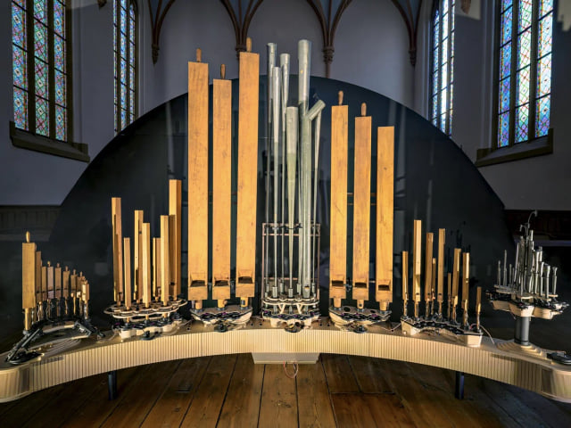 Organism's wooden and metal pipes rising from a curved base in front of stained-glass windows.