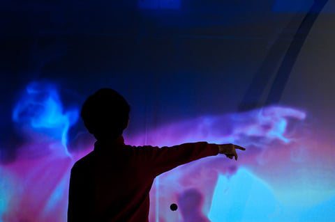 A child pointing at a blue and violet fluid projection in IL Y A.
