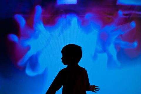 A child's silhouette beside a projection of blue, finger-like fluid forms in IL Y A.