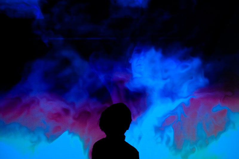 A child's silhouette against a swirling blue and violet fluid projection in the installation IL Y A.
